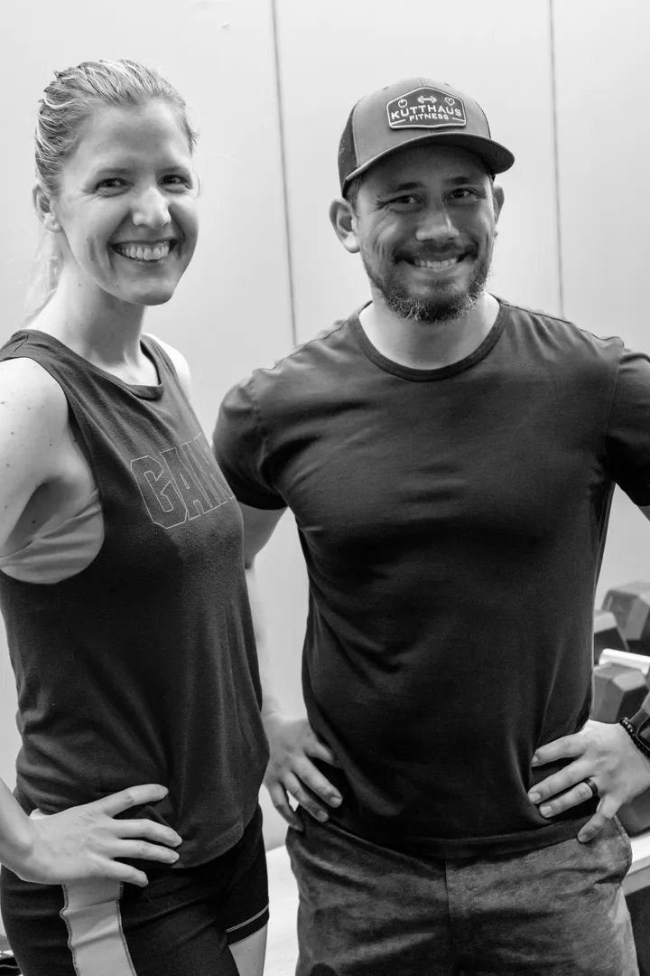 Liz and Sean Kuttner standing together on the gym floor, Sean in a Kutthaus Fitness hat