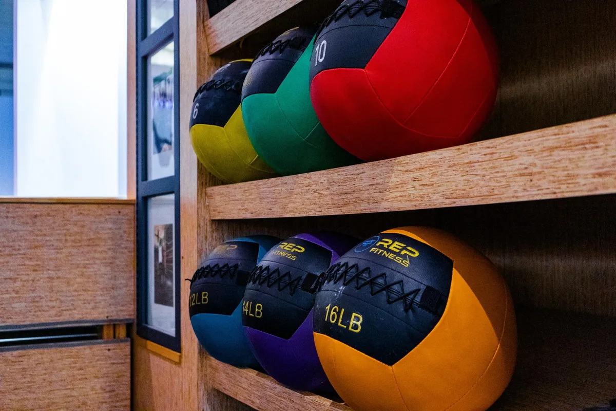 Color-coded medicine balls stacked on wooden shelves at Kutthaus Fitness